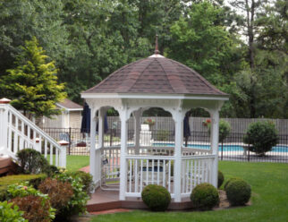 10 Foot White Vinyl Gazebo With Bell Roof With Brown Shingles In A Backyard With A Pool