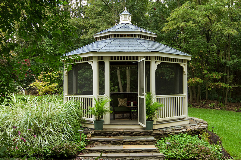 16′ Octagon, Country Style Tan Vinyl Gazebo With Black Shingled Pagoda Roof In A Backyard Garden