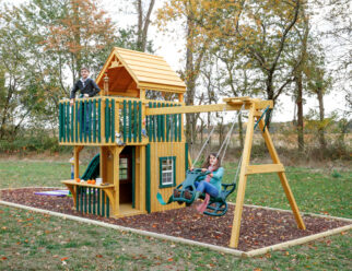 Trading Post 26'x10' Playset with 5x8 Tower, Step Ladder, Hand Rail, Wood Roof, 5x5 Trading Post Enclosure, Green Poly Slats, 10’ Wonder Wave Slide, Spotlight, 3-Position 7’ High Swing Beam, Belt Swing, Child’s Seat with Rope, Plastic Glider, & (6) Anchors