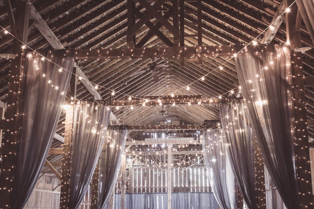 interior of a barn decorated with lights and fabric for a wedding