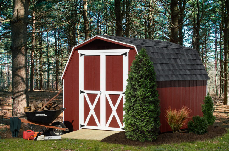 Red Wooden Mini Barn Shed With White Trim Accents Around Door With Black Shingle Roof In A Wooded Backyard