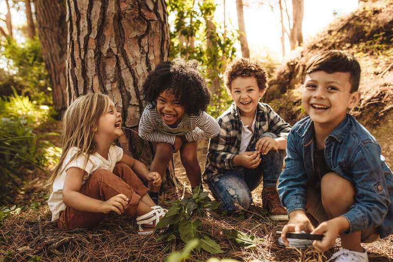 Four children play outdoors in the woods