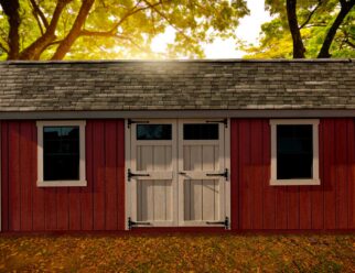 Red backyard monterey shed with two windows and barn style doors in front of a setting sun