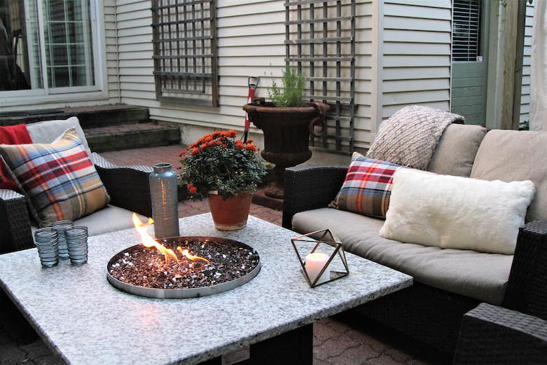 A cozy fire pit is lit with comfortable chairs sitting around it on a Fall patio.