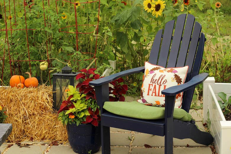 A colorful "hello fall" pillow sits on a black outdoor chair with a green cushion.