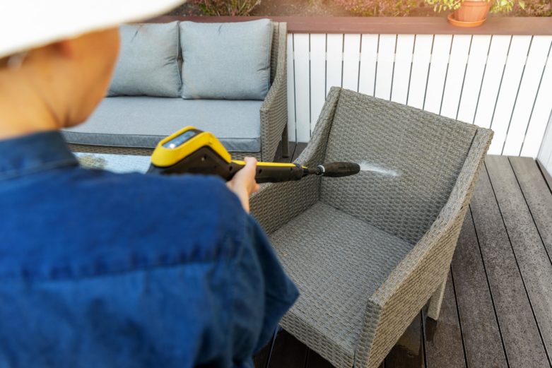 A woman power washes a plastic poly chair.