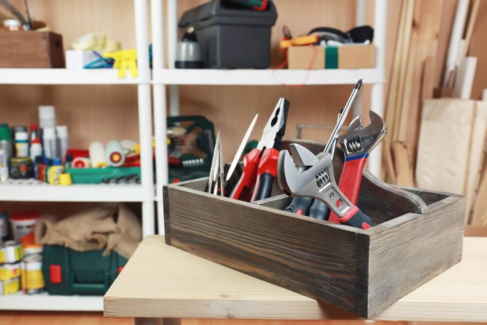 Box of tools in a wooden tool box sitting in a garage.