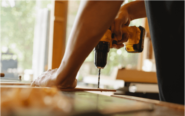 A picture of a man using a drill on a wooden board.