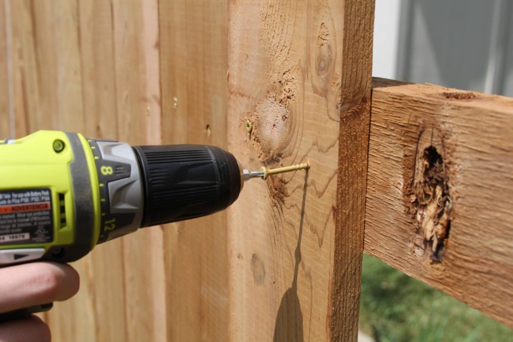 A close up photograph of an electric drill screwing a nail into a wooden plank showcasing the importance of swing set maintenance.