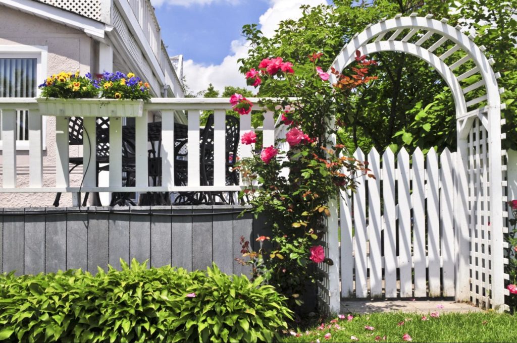 A white picket garden arbor with a gate, showing the beautiful possibilities options for garden arbor ideas.