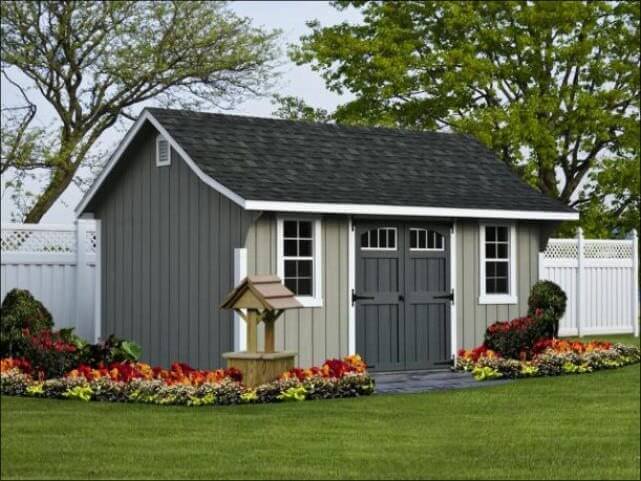 Gray Cape Elite Shed With Grey Doors And A Black Shingle Roof With A Wishing Well Near The Entrance