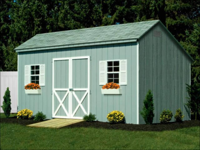 Green Wooden Carriage Shed With White Accents Around Doors and White Shutters With Flower Boxes