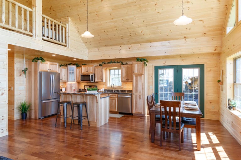 The interior of a log cabin home design that highlights the kitchen area, with an island and dining table. 