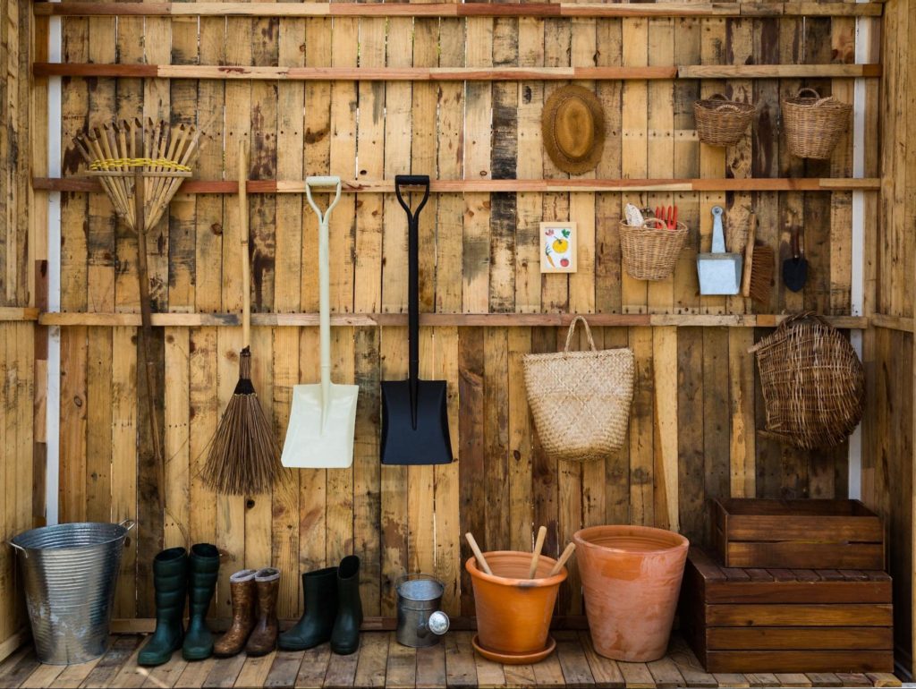 One side of a wooden shed with lots of gardening materials, boots, buckets, and wooden crates. 
