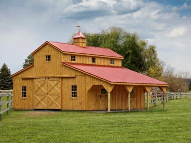 A large wooden horse barn with a red metal roof and double sliding doors.