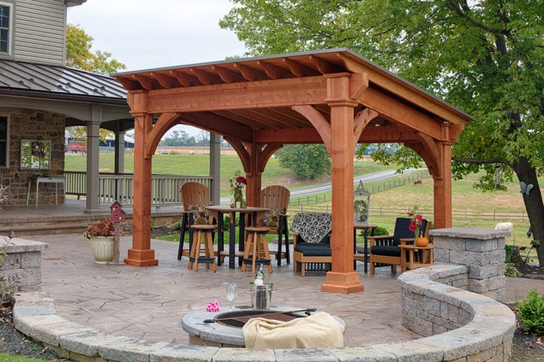 A free-form patio with a pergola on top and a table set underneath.