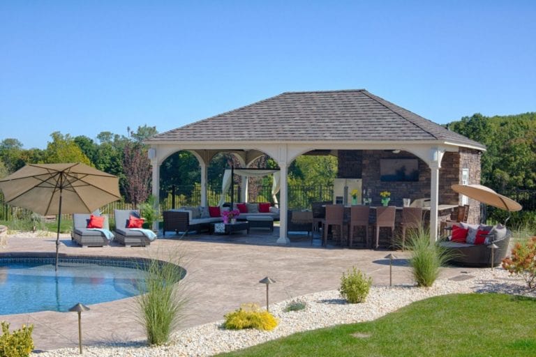 A pergola with an outdoor kitchen underneath and a pool on the side.