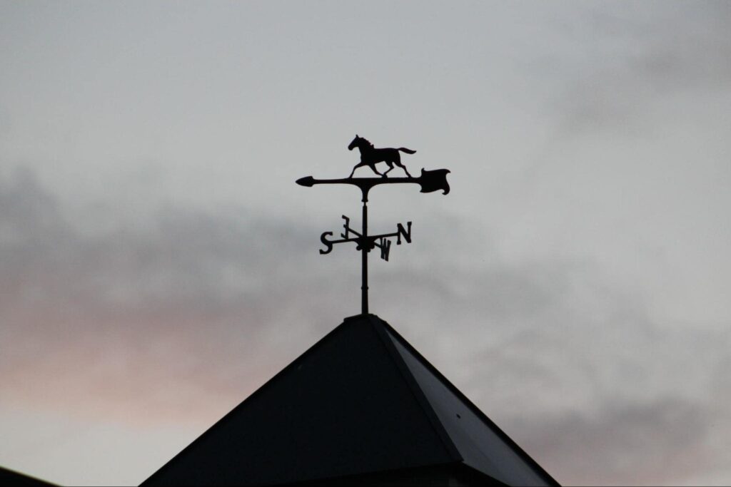 a silhouette of a weathervane decorated with an arrow and a horse. 