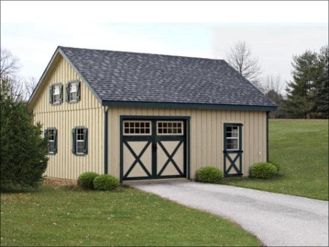 A tan garage with green trim and small shrubs surrounding the base.