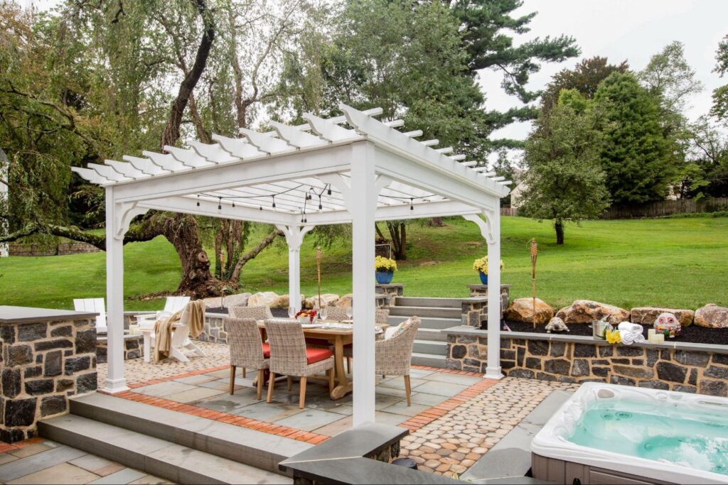 a vinyl pergola with a lounge area underneath and a hot tub next to it.