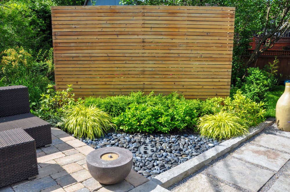 Privacy wall set up around a patio with bushes in front of it