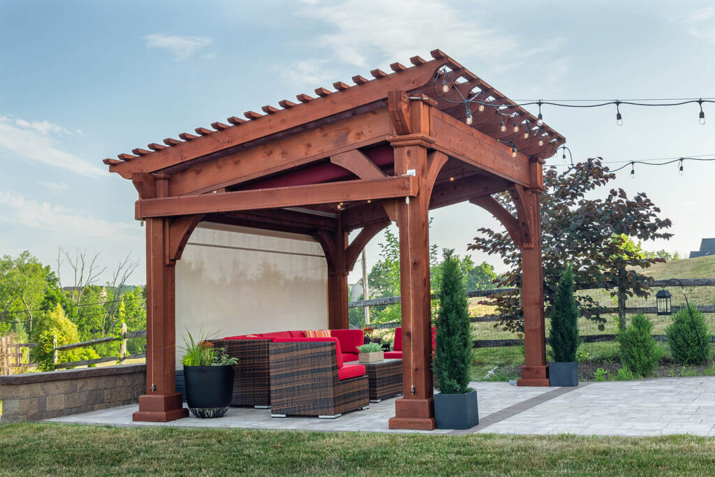 Wooden Santa Fe style pergola with a privacy curtain. It sits on a patio with outdoor seating beneath