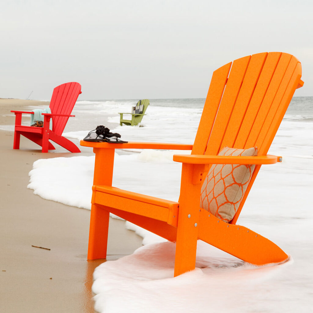 An orange Adirondack chair sitting in the sand at the beach with waves lapping at it's legs