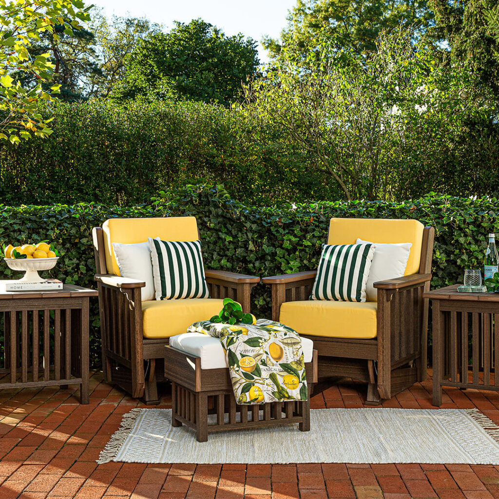 Two patio furniture armchairs with yellow cushions and side tables on a brick walkway